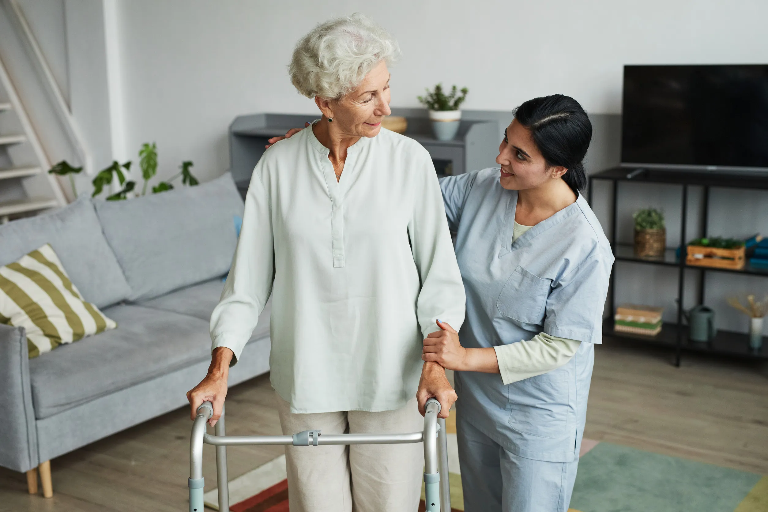 Waist up portrait of smiling female nurse helping senior woman using mobility walker in retirement home, copy space