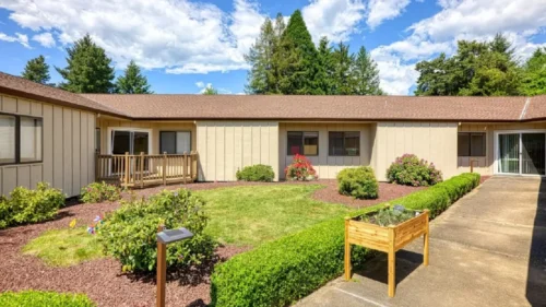 A courtyard with a grassy area, a concrete path, and a building with a wooden deck and tan siding