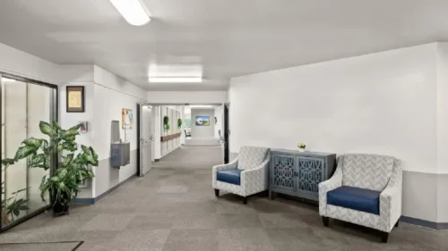 A hallway intersection with two patterned armchairs, a decorative console table, and an entryway to another hallway