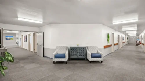 An indoor hallway intersection with gray carpet, a white and gray console table, and two patterned armchairs